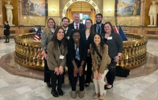 A group of student doctors and KHSC – KansasCOM staff and faculty gather in the Kansas Statehouse rotunda.