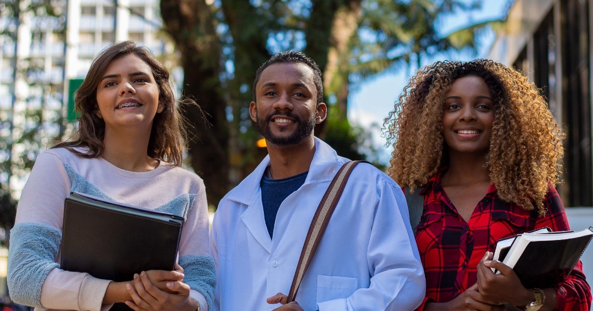 Three people holding books and documents smile at something off-camera.