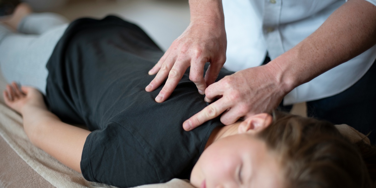 A pair of human hands massage a young person's back in close-up.
