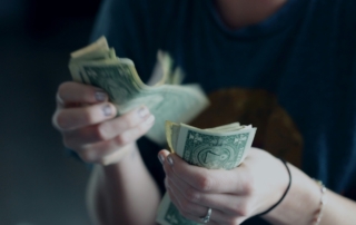 In close-up, a person counts a stack of American dollar bills held in their hands.