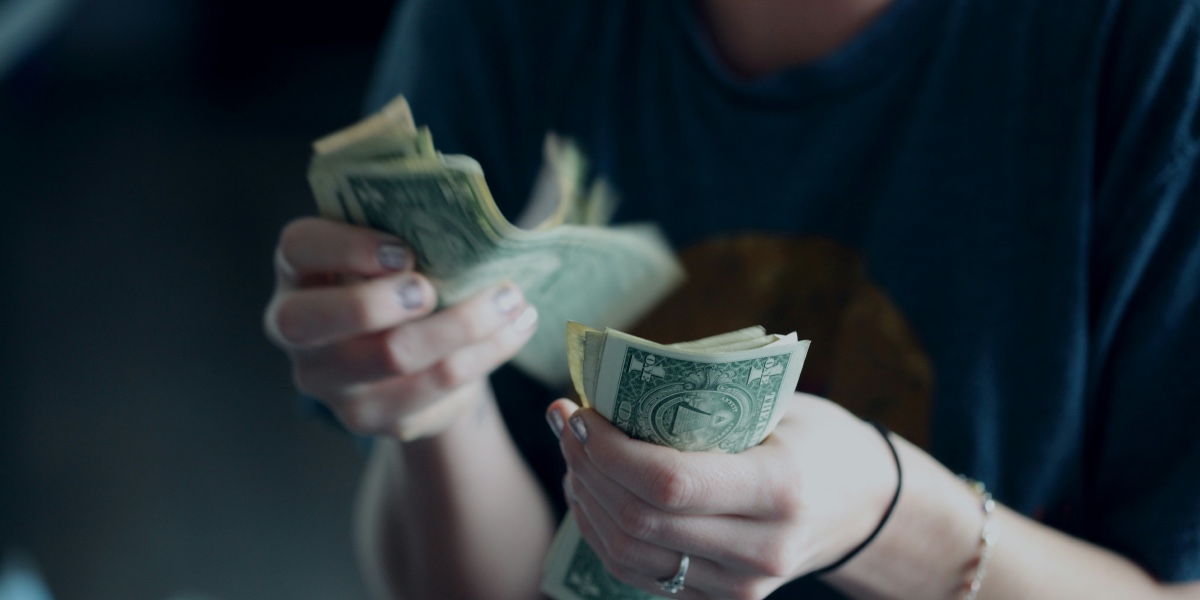 In close-up, a person counts a stack of American dollar bills held in their hands.