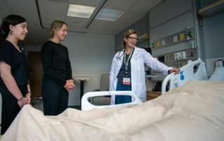 Dr. and two students meet with patient in hospital bed.