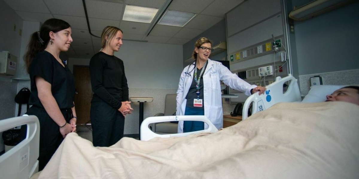 Dr. and two students meet with patient in hospital bed.