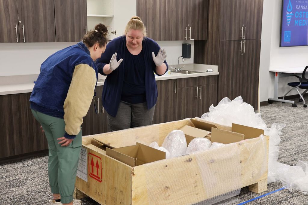 Two people appear to be filled with glee while looking into a wooden shipping box on the ground before them.