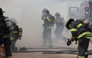 Firefighters walk around a smoky lot.