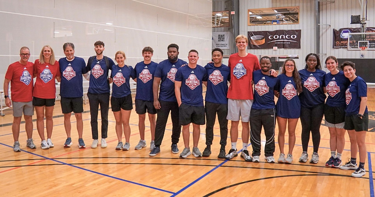 KansasCOM studnets pose with Gradey Dickcamp on a basketball court.